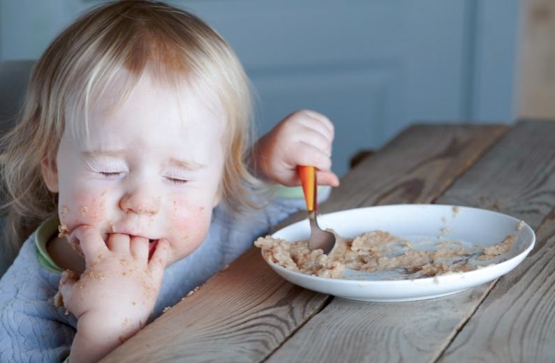 スプーンを握りながら手づかみ食べする子ども